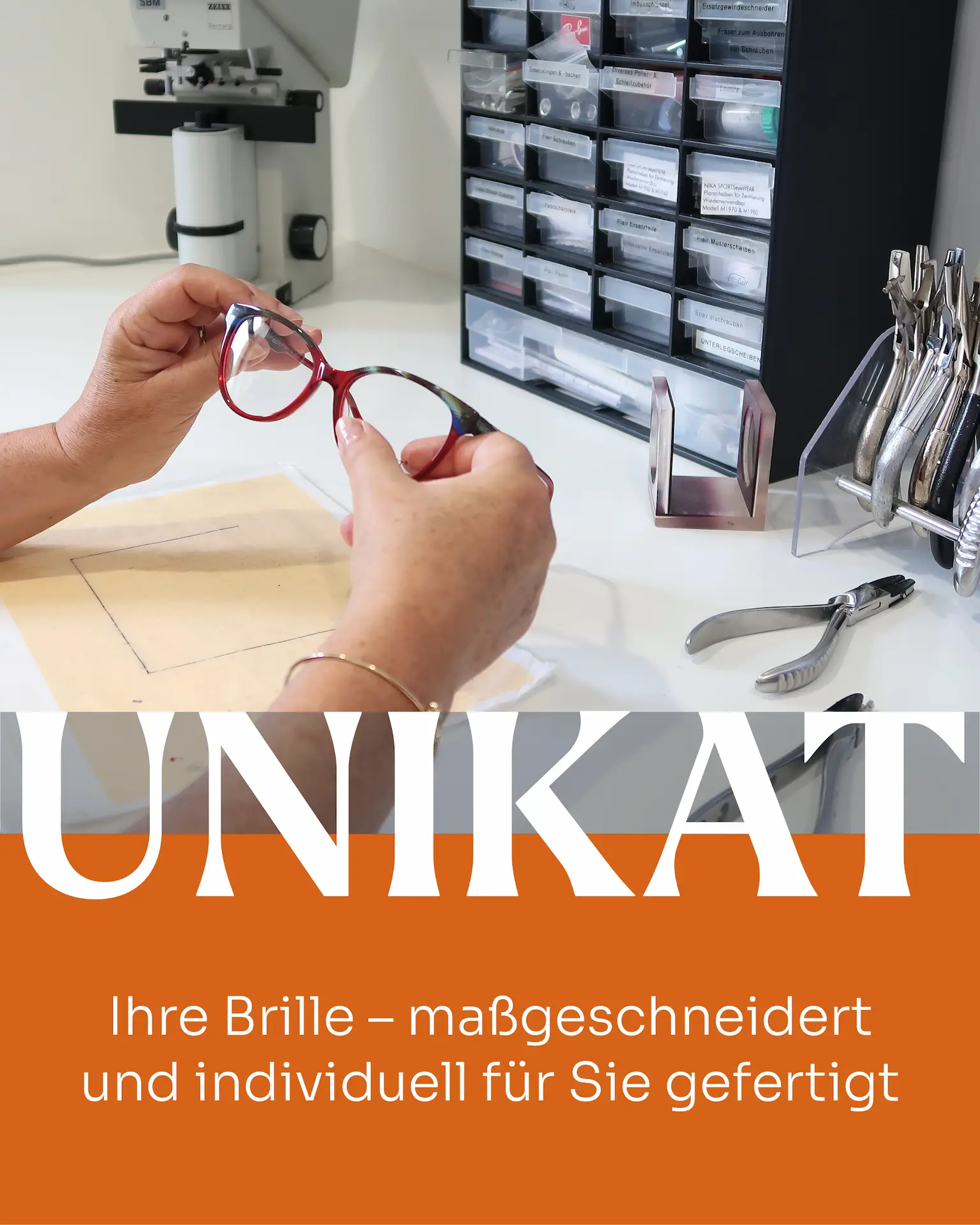 Bildauschnitt aus der Brillenwerkstatt - 2 Hände halten eine Brillenfassung - auf dem Schreibtisch sind verschiedene Zangen zu sehen